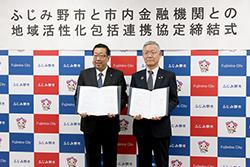 市長と眼鏡をかけてグレーのネクタイを身に着けている市内金融機関代表の方が締結書を持って横並びで立っている写真