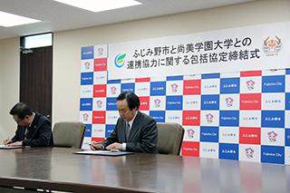 締結式にて、2人の男性が締結書にサインをしている写真