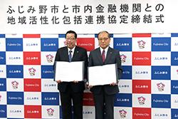 市長と赤いネクタイを身に着けている市内金融機関代表の方が締結書を持って横並びで立っている写真