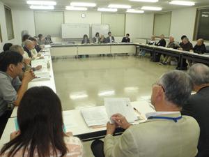 会議室で第3回全体会議が行われていて参加者の人達が資料に目を通している写真