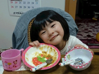 女の子がテーブルの上の空になったお皿を2枚両手で持って見せている写真