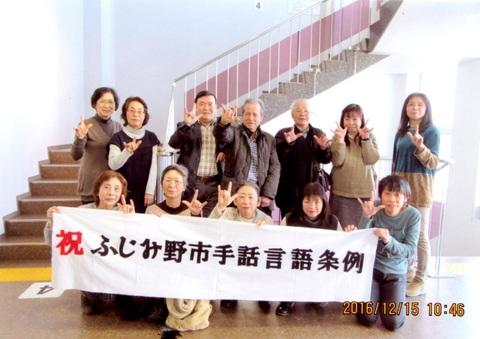 祝ふじみ野市手話言語条例と書かれた横断幕を掲げる手話をしている男女が写っている条例可決時の写真