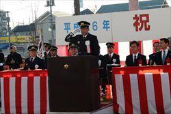 紅白の横断幕が長机の周りに貼られており、壇上に立っている市長が敬礼をしている写真
