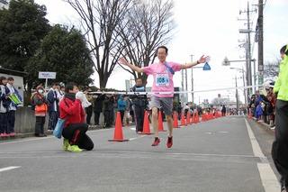 ピンクのTシャツを着たランナーがゴールテープを切っている写真