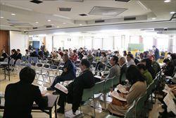 公開討論会の沢山の参加者が、会場に設けられている椅子に座っている様子の写真