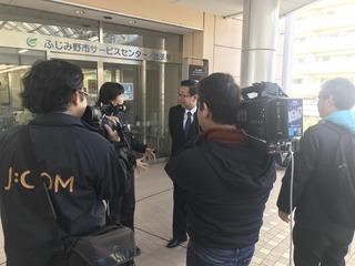 サービスセンターの玄関で撮影をされている市長をカメラマンの後ろから写した写真
