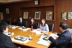 机の上にお弁当を広げて、市長が話をしているのを若手職員の皆さんが、聞いている様子の写真