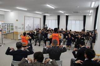 参加者達が椅子に座り肩に手を置いて「ふじみんぴんしゃん体操」をしている写真