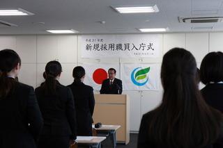 演壇に立ち話をする市長と起立したまま話を聞いている新規採用職員の写真
