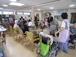 中丸デイサービスセンターで、車いすや、椅子に座る高齢者の前に立ち、話をする市長の写真