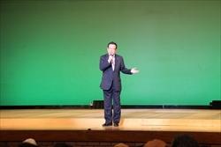 大井芸能協会舞踊まつりの舞台上で、市長が右手にマイクを持ち、左手を横に出している写真