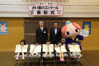 5人の子ども達がメダルを首からかけて賞状を胸の前で持って椅子に腰かけ、その後ろに市長とスーツ姿の男性とふじみんが立っている集合写真