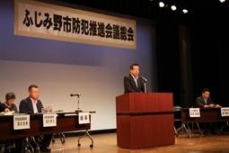 「ふじみ野市防犯推進会議総会」の横断幕の前で、市長が演壇で話をしており、演壇の横には長机が置かれ、関係者の方々が座っている写真