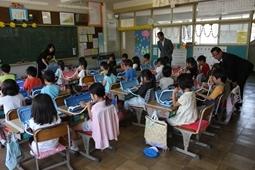 子供達がピアニカを演奏している様子を机の横に立ち、腰を低くして見学している市長の写真