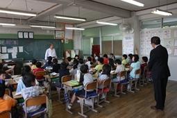 先生が前に立ち話をしている教室の一番後ろに立ち見学している市長の写真