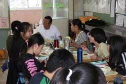 赤や青の水筒が置かれている女の子のグループと一緒に給食を食べている市長の写真