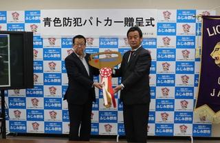 「青色防犯パトロールカー贈呈式」と書かれている横断幕の前で、大井ライオンズクラブの関係者の方と市長が紅白のリボンのついた大きな金色のレプリカキーを持って写っている写真