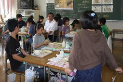 給食の時間に後ろのグループの茶色のパーカーを着た女の子の質問を聞いている市長の写真