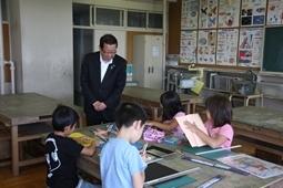 児童4人が一つの大きな机でものさしや紙を使い工作している所を市長がのぞきこんでいる写真