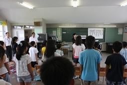 起立をして前方に市長と関係者、その中央に立つ先生の方に身体をむけている児童達を教室の後方から全体的に写した写真