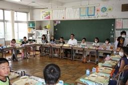 教室全体に机を並べ、黒板の前の子供達の間に市長も座りみんなで給食がはじまるのを待っている写真