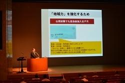 舞台上のライトアップされた演台に立ち、話をする市長の写真