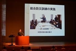 プロジェクタースクリーンに映る写真の横で、市の取り組みについて話をする市長の写真