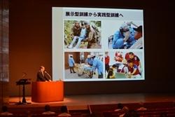 プロジェクタースクリーンに映し出された写真と、演台に立ち、話をする市長の写真