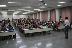 机に座っている入学した生徒に先生が話をしている写真