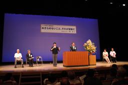 舞台の演題で挨拶する市長の横で女性が手話通訳をしている写真