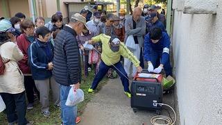 発電機のエンジンをかけている男性を周りで見ている人達の写真