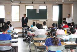 可動式の黒板の前で立って市長が話しをしているのを、着席して話しを聞いている子供たちの写真
