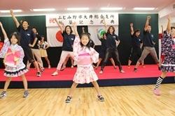 ステージ上で、右手を上げて両足を大きく広げてポーズを決めている男女と浴衣を着た女の子の写真