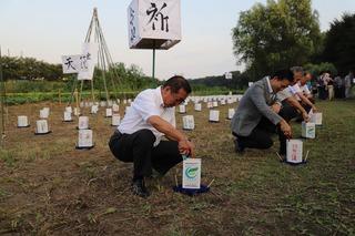 新河岸川のほとりに沢山の燈籠が並べられており、市長と祭りの参加者が燈籠に火を灯している写真