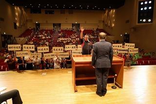 チーム名が書かれたプラカードを持って舞台前に集まっている各チームの代表者と、壇上の市長の前で選手宣誓をしている代表者の男性の写真