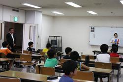 着席した子供たちが、前に立つ女性を注目している写真