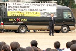 横断幕が張られた、黒いワゴン車の前に立ち、話をしている市長の写真