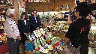 丸康園さんの店内で、店主の白髪の男性と市長、スーツを着た女性が話ている様子を撮影してる現場の写真