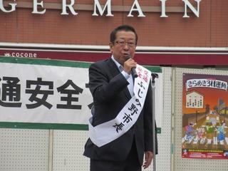 東入間地区交通安全フェアの会場で市長が「ふじみ野市長」と書かれている白いタスキを肩にかけてマイクを持って話をしている写真