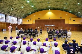 体育館の中での式典に参加している人達、野球のユニフォーム姿の人達は後方に座っている写真