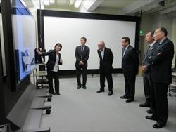 株式会社KDDI研究所訪問時に無響室での実験の説明を立って聞いている市長たちの写真
