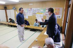 農作物の品評会にて生産農家の男性が市長より表彰を受けている写真