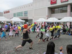 ぶんぶんまつりの会場にて子ども達が手に黄色や黄緑、紫色のボンボンを手に持ってダンスを踊っている写真