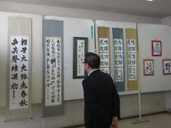 掛け軸に書かれている書の作品が展示されており、市長が両手を後ろで組んで、じっくりと見ている写真