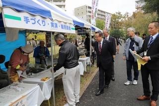 出店で買い物をしている男性を後ろからのぞき込む市長の写真