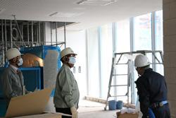 ヘルメットとマスクを付けた市長が、工事担当者より増築現場の庁舎内の説明を受けている写真