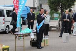 市長が青いタスキを肩にかけてマイクを持って話をしている写真