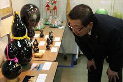 黒光りしている大きなひょうたんが展示されており、市長が腰をかがめてひょうたんを見ている写真