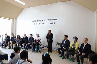 「ふじみ野市立スポーツセンターアーチェリー初射ち・体験会」と書かれてた紙が壁に貼ってあり、その前で市長が立って挨拶をしており、その横には平澤 奈古さんや関係者の方々が座っている写真