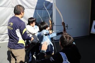 アーチェリー体験に参加している子ども達が、関係者の方も教えてもらいながら、的に向かってアーチェリーを構えている様子の写真